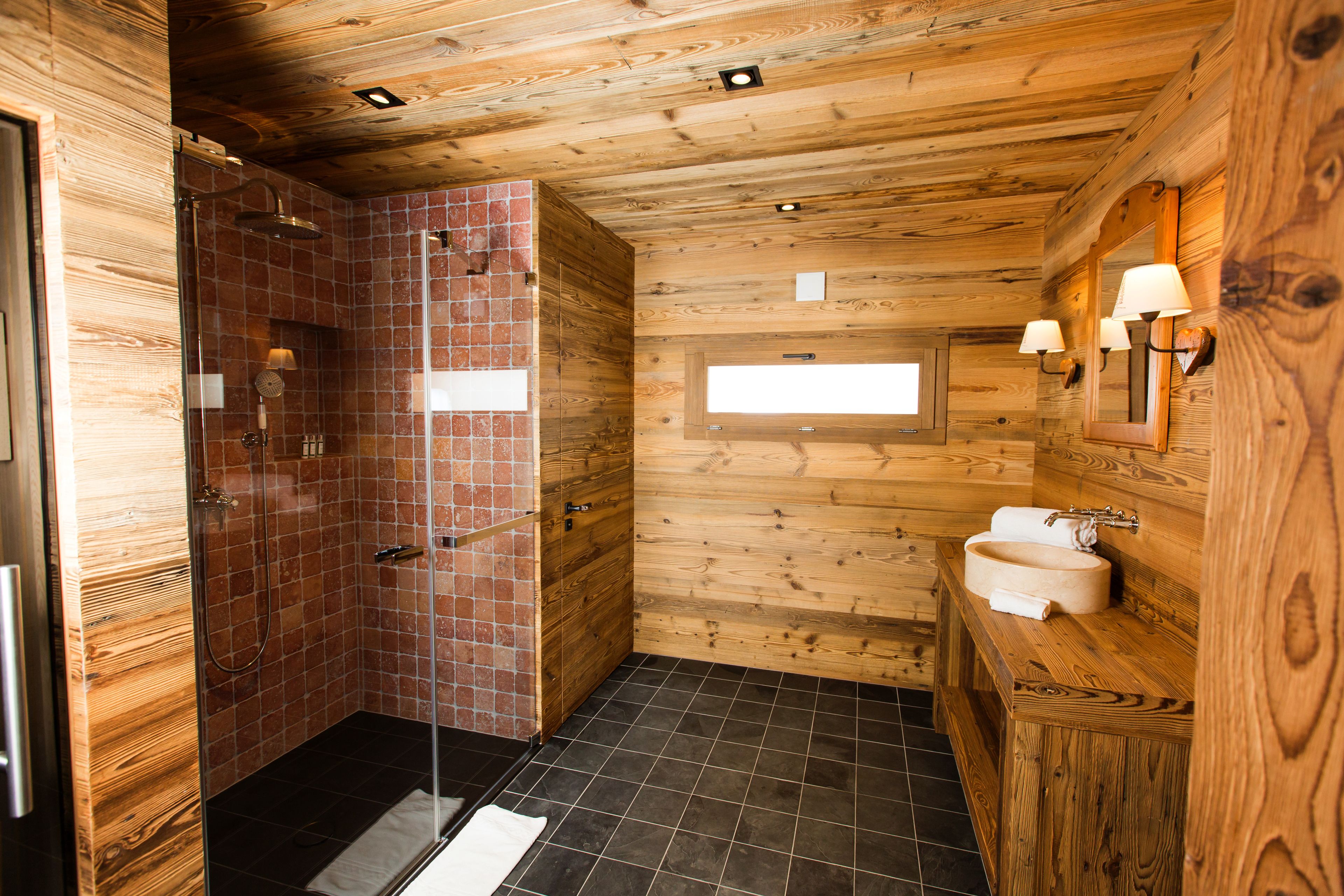 Baño de cabaña de madera con ducha, lavamanos y ventana.