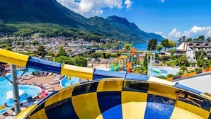Un parque acuático con una piscina grande, toboganes y vistas a un pueblo y montañas al fondo.