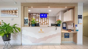 Un comptoir d’accueil d’hôtel doté d’un écran numérique affichant les prévisions météorologiques, un bureau d’accueil et des plantes en pot.