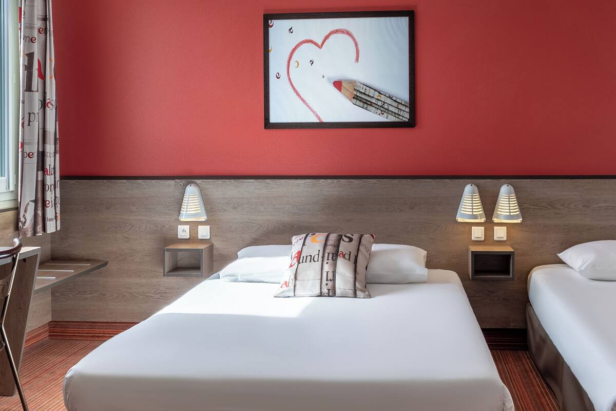 Habitación de hotel con una cama grande, dos mesitas de noche con lámparas, un cabecero de madera y una pared de acento roja.