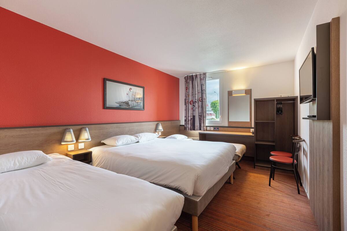 Habitación de hotel con dos camas, cabecera de madera, un escritorio con silla, un espejo y un armario.