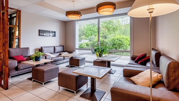 Un espace de détente moderne, doté de canapés, de tables et d’une grande fenêtre donnant sur un paysage verdoyant.