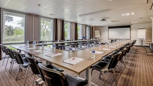 Une salle de conférence équipée de longues tables, de chaises, de bouteilles d’eau et d’écrans de présentation.