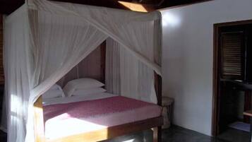 A single bed with a canopy in a room with a wooden floor and a door to the right.