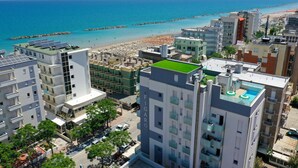 A high-rise building with a rooftop pool and solar panels, overlooking a beach and the sea. - Amadei Hotel Figaro & Apartments (Pesaro)