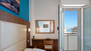 A hotel room with a bed, a desk, a chair, a mirror, and a balcony with a view of the sea. - Amadei Hotel Figaro & Apartments (Pesaro)