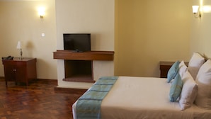 Habitación de hotel con cama, televisor sobre un mueble de madera, escritorio con lámpara y mesita de noche.