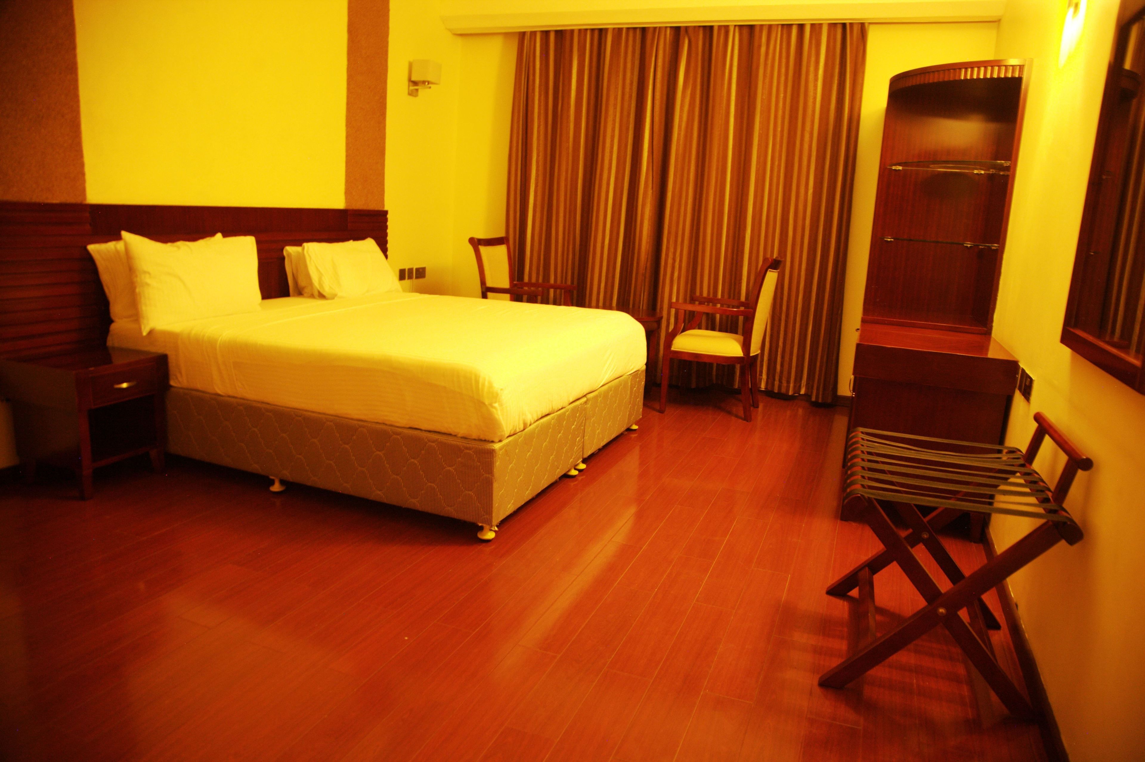 A hotel room with a large bed, wooden headboard, a chair, a wooden bench, and a wardrobe.