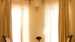Una habitación con dos sillas de madera y una pequeña mesa, un florero con flores rojas, y una lámpara en la pared.