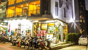 A multi-story building with a ground-floor shop, balconies, and a parking area with motorcycles.