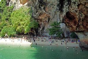 A crowded beach with people swimming and sunbathing, surrounded by rocky cliffs and lush greenery. - The Capuchin Hotel (Krabi)