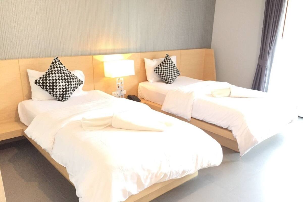 Hotellihuoneessa on kaksi sänkyä, joissa on valkoiset lakanat ja mustavalkoiset kuviolliset tyynyt. Sänkyjen välissä on yöpöytä, jossa on lamppu.