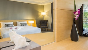 A hotel room with a bed, a chair, a desk, a lamp, and a vase with flowers.