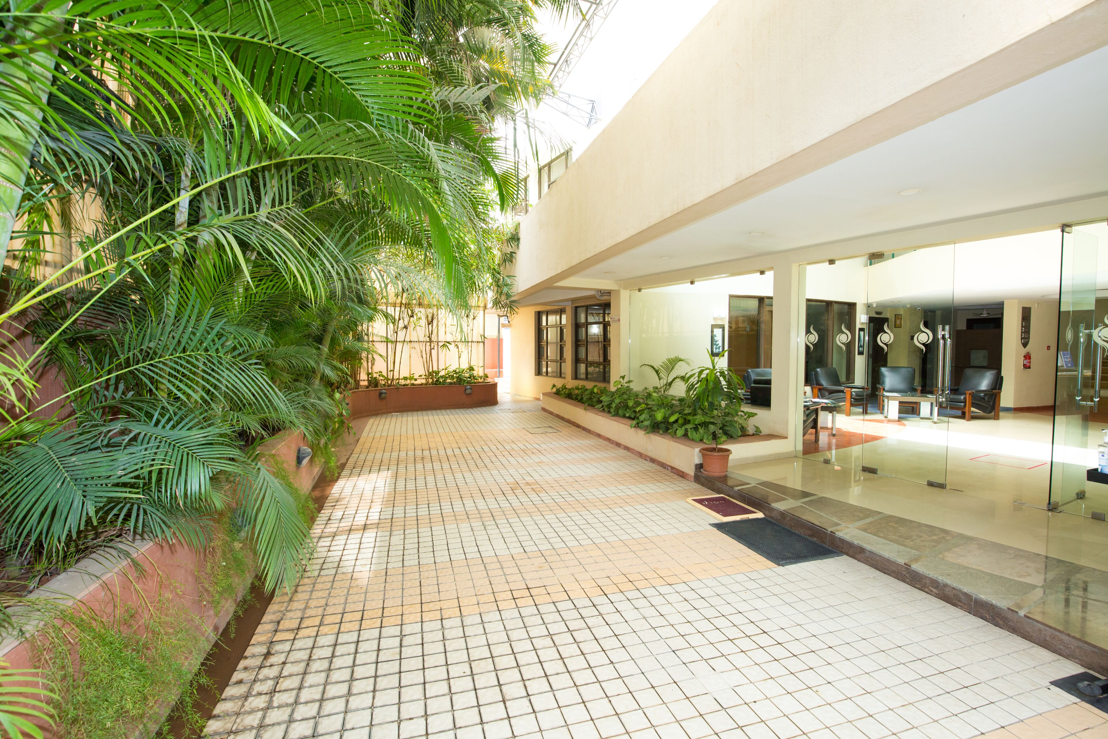 A tiled courtyard with a glass door entrance, potted plants, and a seating area with chairs.