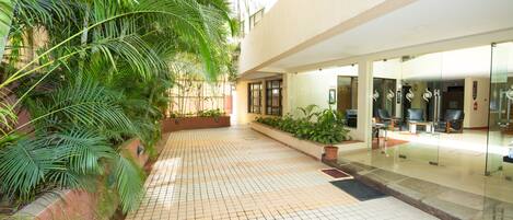 A tiled courtyard with a glass door entrance, potted plants, and a seating area with chairs.