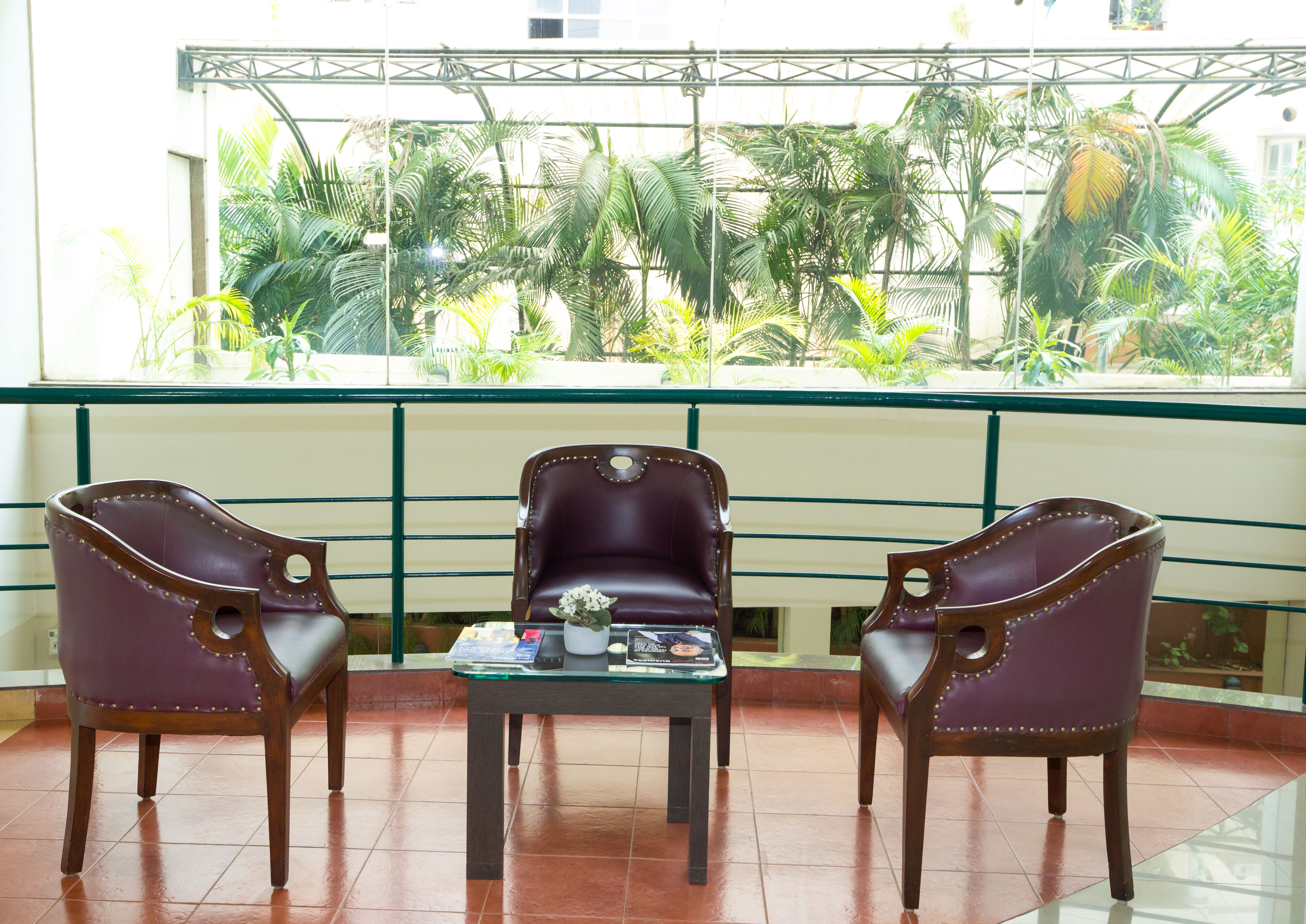 A balcony with three leather chairs and a small table, overlooking a lush garden.