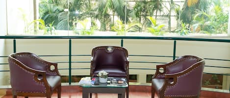 A balcony with three leather chairs and a small table, overlooking a lush garden.