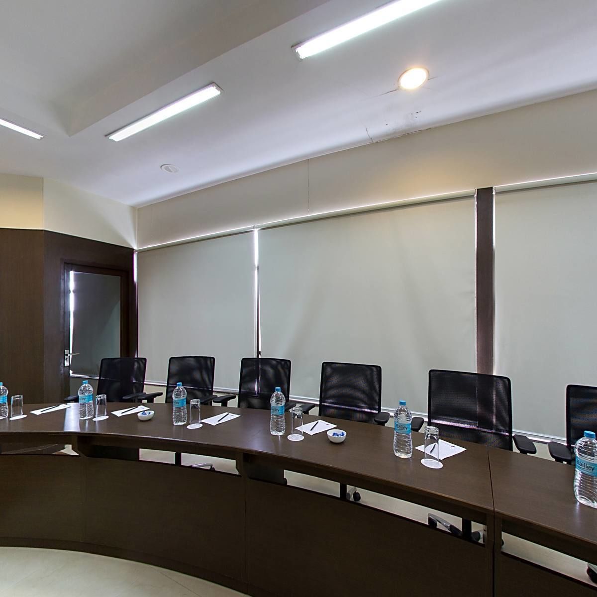 Una sala conferenze con un lungo tavolo, sedie, bottiglie d'acqua e uno schermo per proiettore.