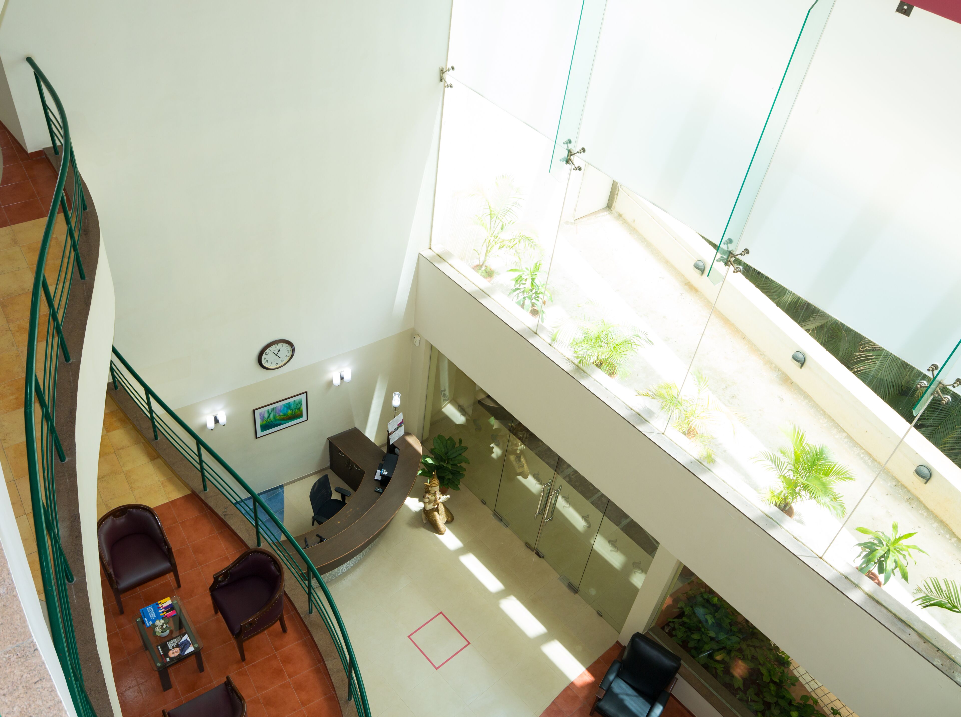 A spacious lobby with a high ceiling, a reception desk, seating area, and a view of the outdoor balcony with plants.