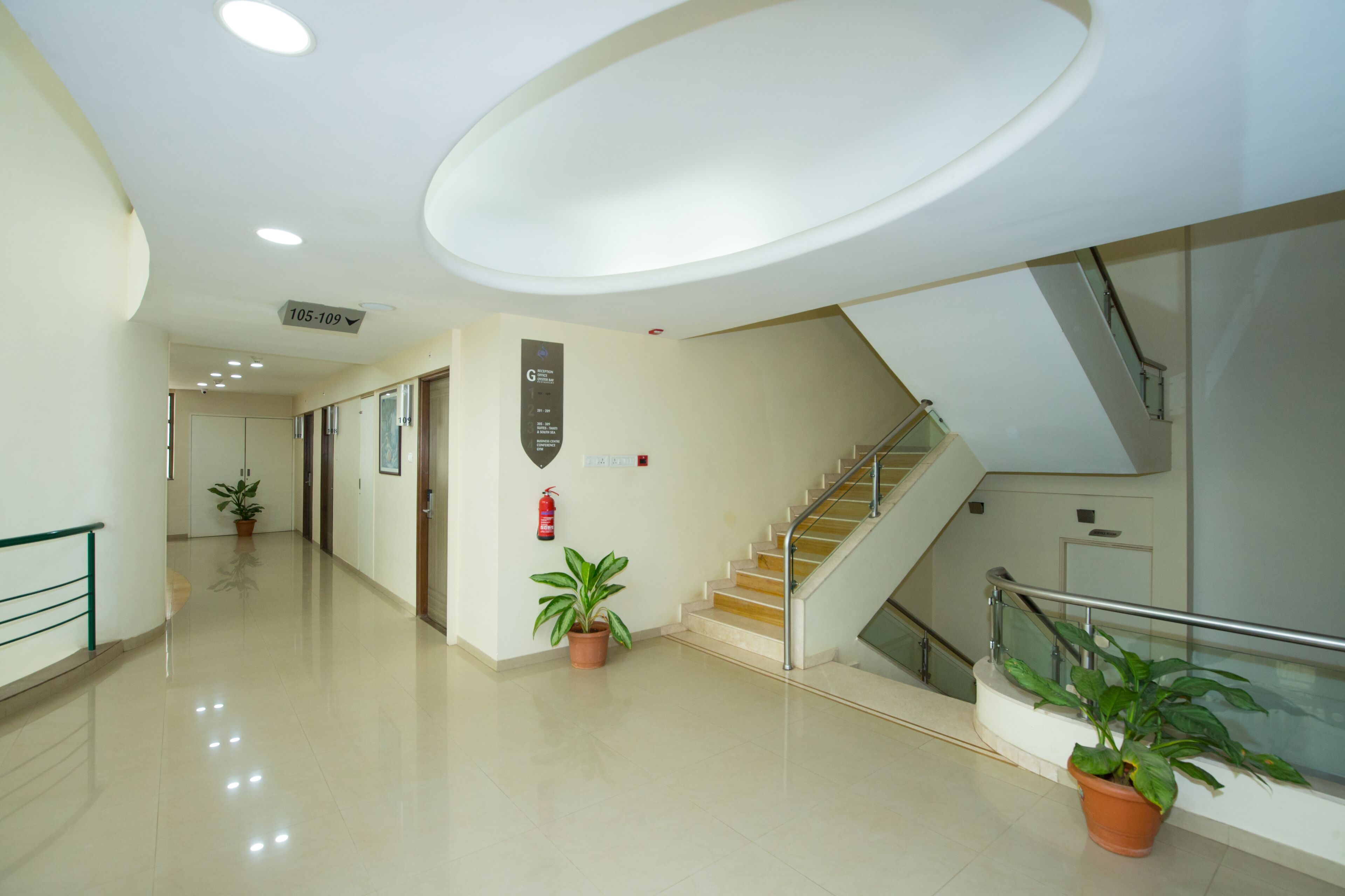 A modern hotel corridor with a staircase, potted plants, and a fire extinguisher on the wall.