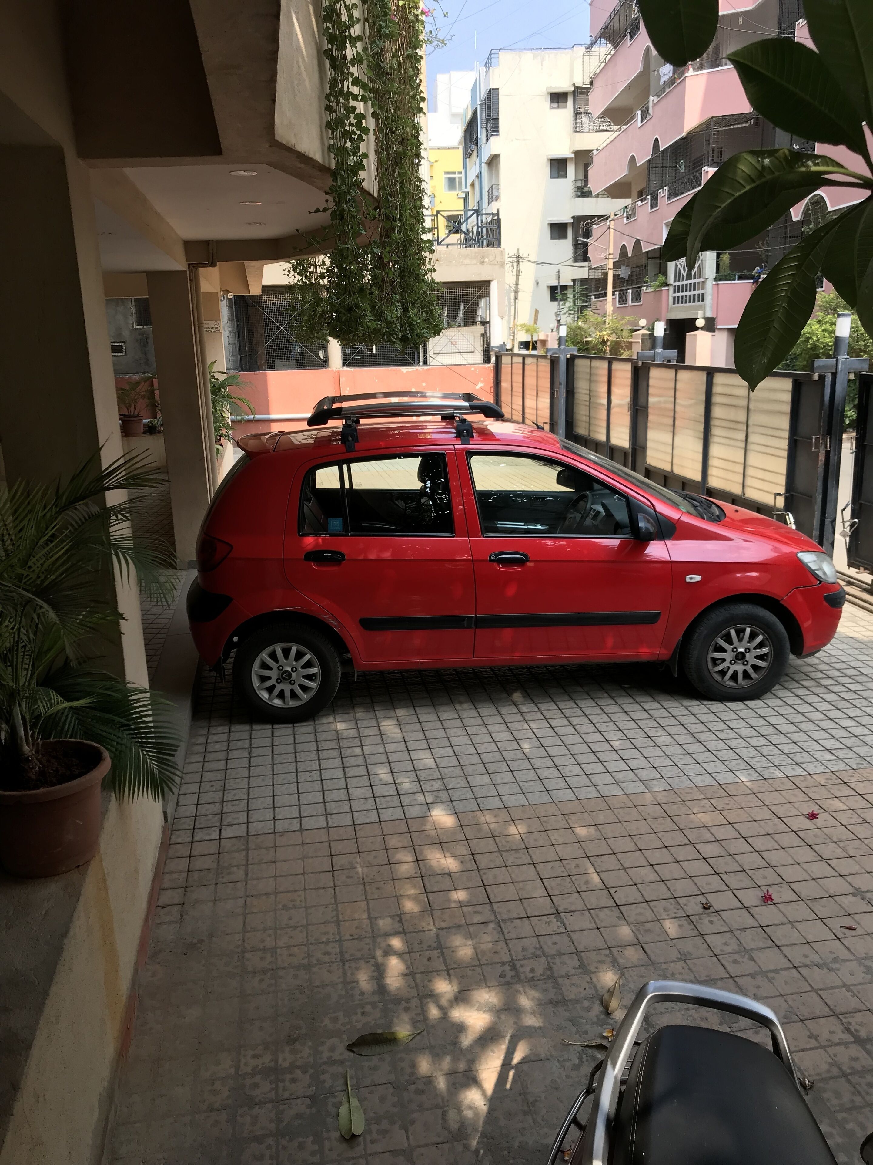 A red car parked on a tiled driveway with a potted plant on the left.