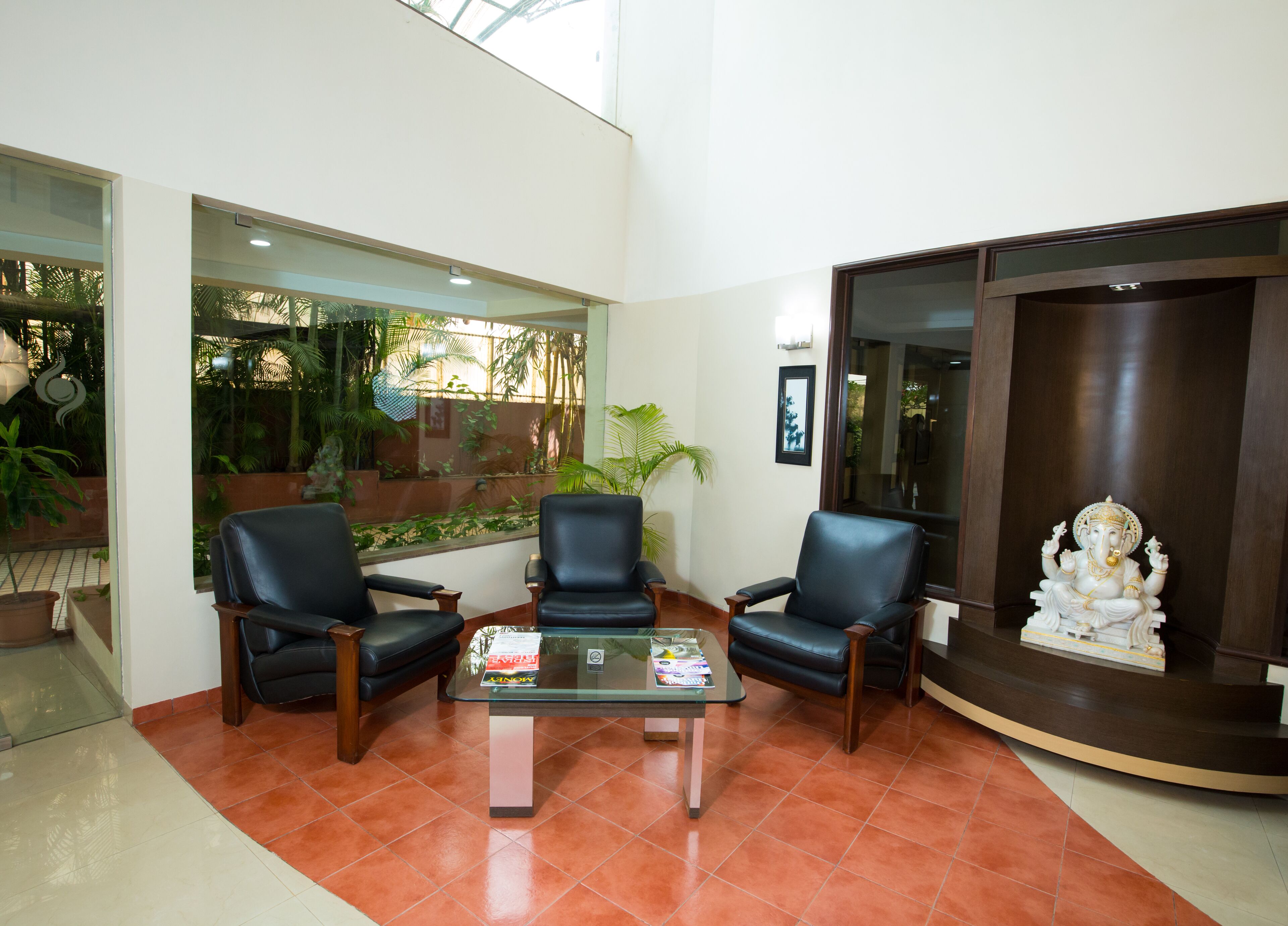 Un área de recepción con dos sillones de cuero negro, una mesa de vidrio con revistas y una estatua de una deidad.