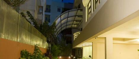 Een modern gebouw met een gebogen glazen balkon, een verharde looppad en een goed verlichte ingang.