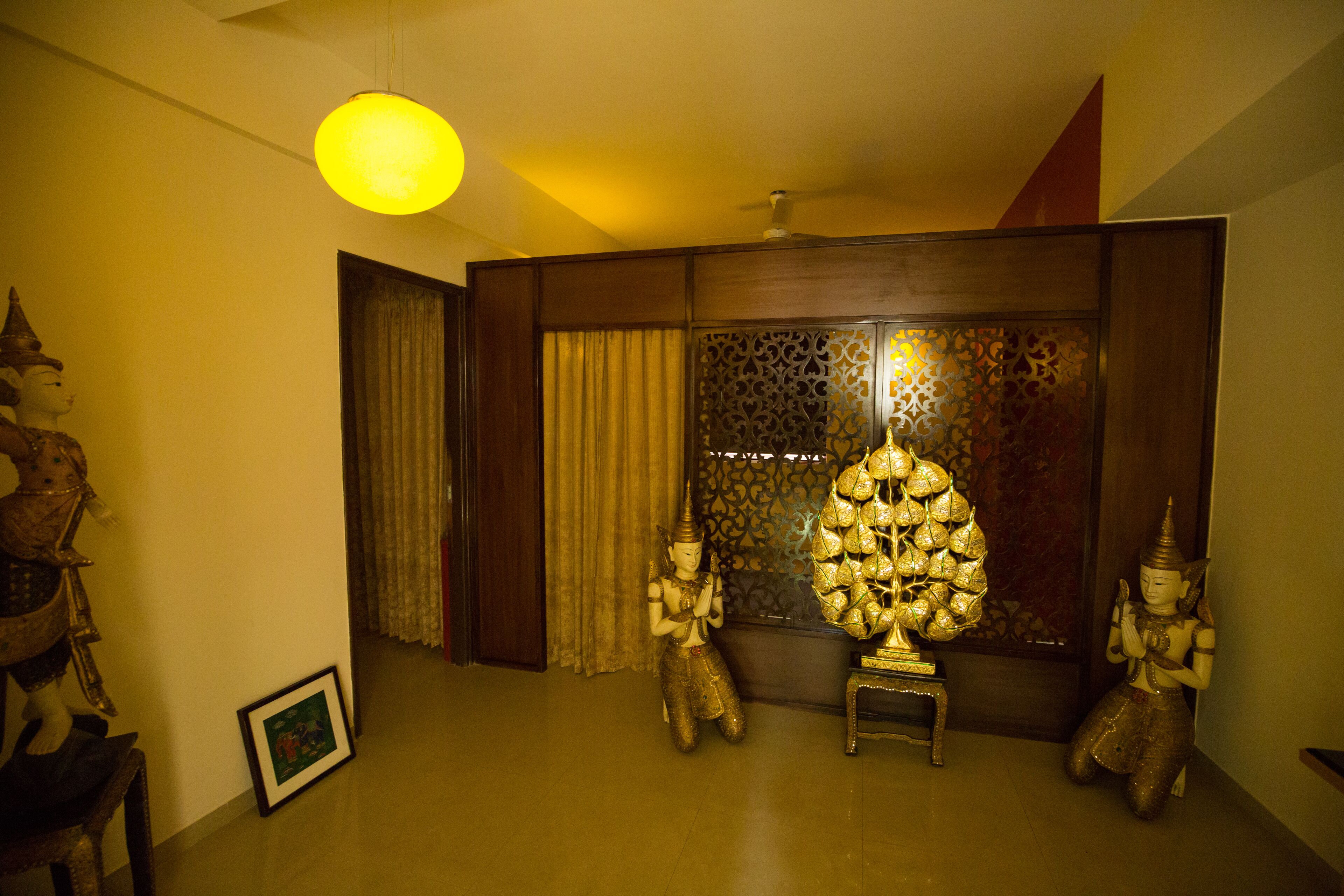Una habitación con un panel de madera tradicional, una estatua de Buda y un objeto dorado decorativo sobre una mesita.