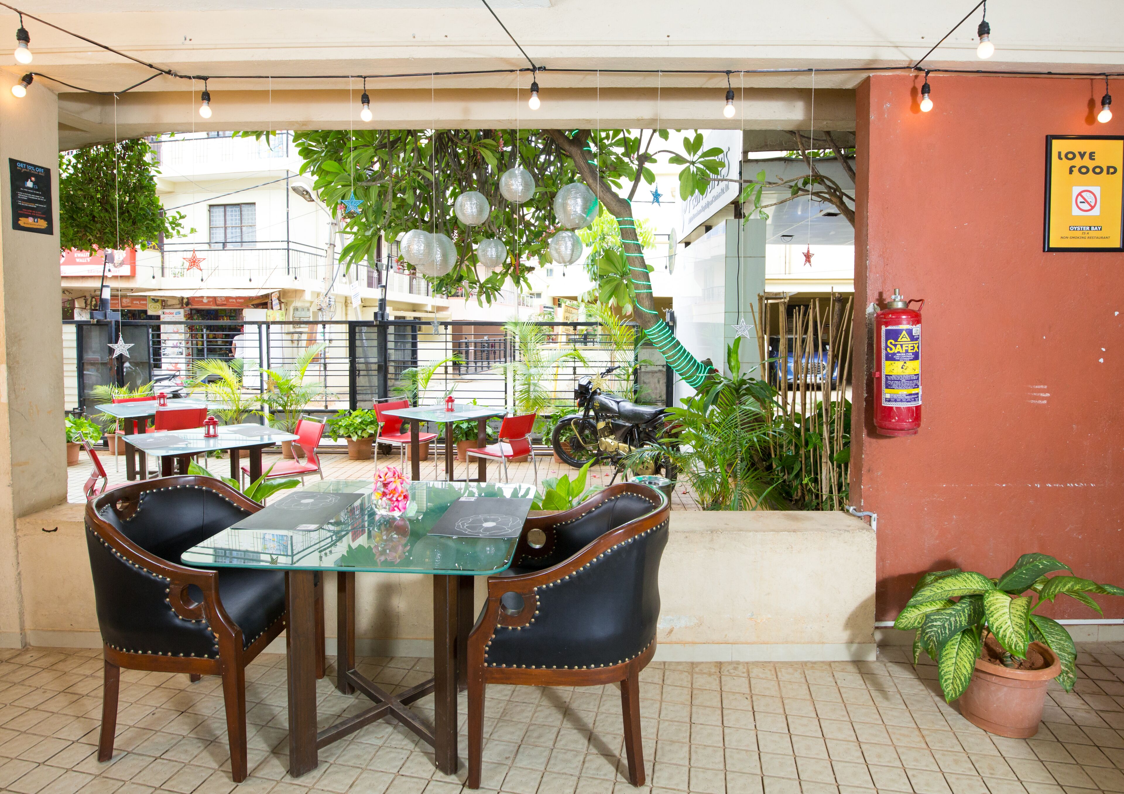 An outdoor dining area with tables and chairs, surrounded by potted plants and hanging decorations.