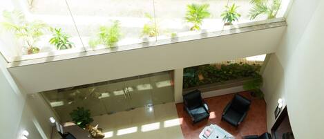 A spacious indoor area with a glass ceiling, a seating area with chairs, a coffee table, and a reception desk.
