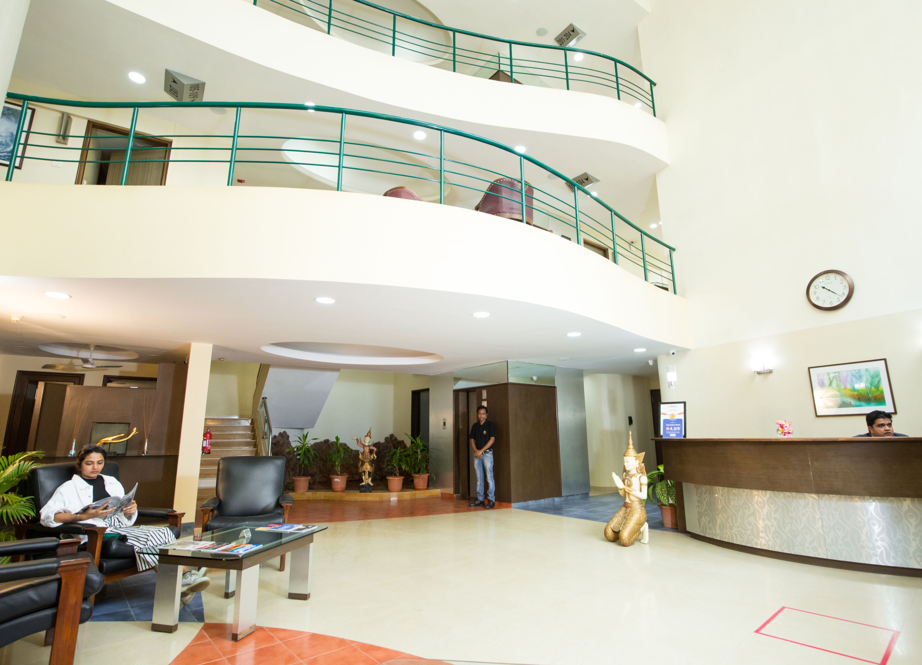 A hotel lobby with a reception desk, seating area, staircase, and decorative statues.