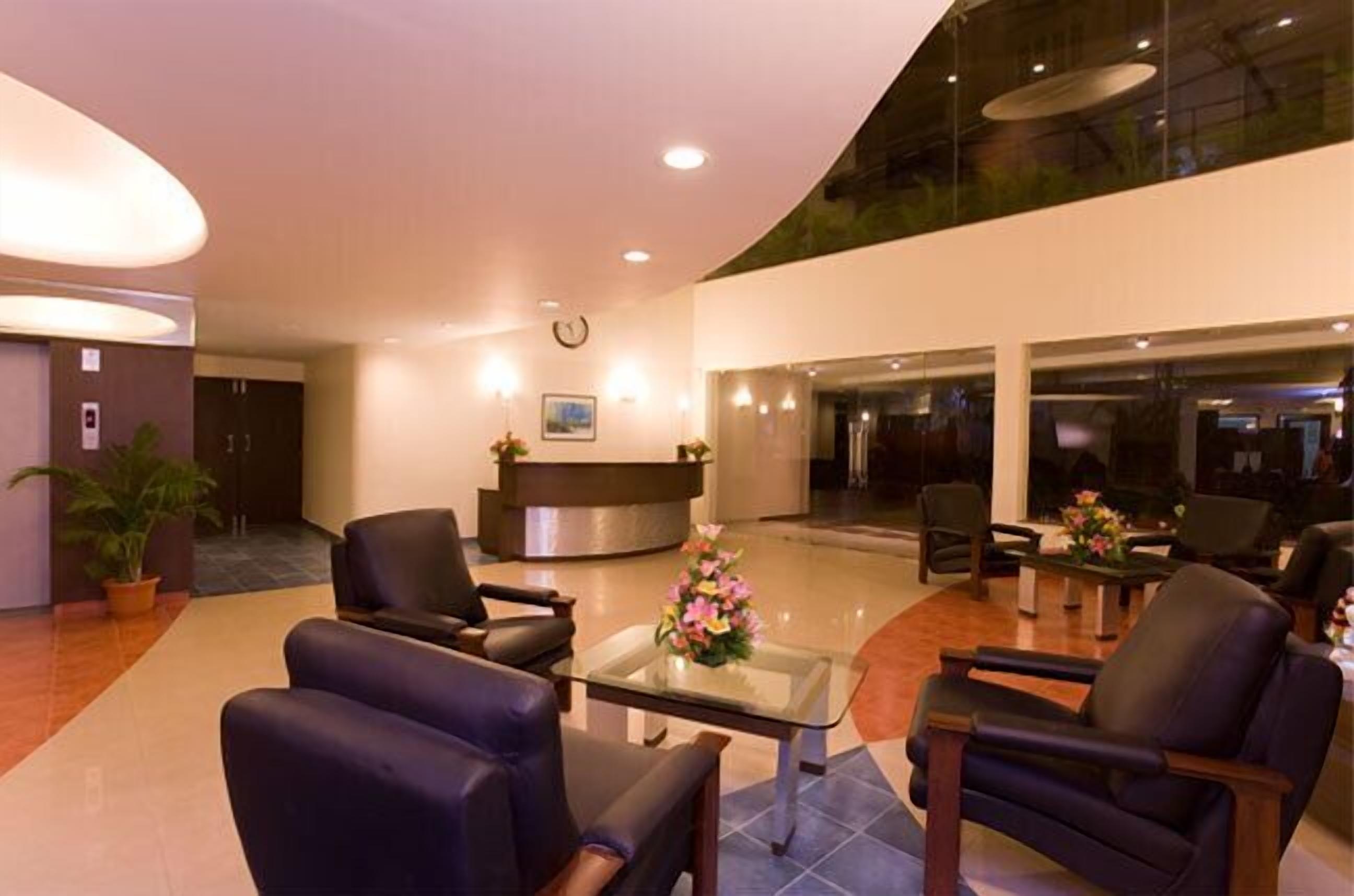 Een moderne lobby met een receptiebalie, een zithoek en een glazen bijzettafeltje met bloemen.