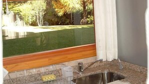 Una cocina con marco de ventana de madera, un lavamanos de acero inoxidable y un escurreplatos.