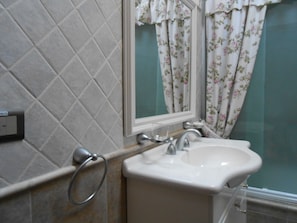Une salle de bain avec un lavabo blanc, un miroir et un rideau de douche orné de motifs floraux.