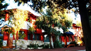 Un edificio de color rojo y blanco con base de piedra, una puerta de madera y un árbol grande al frente.