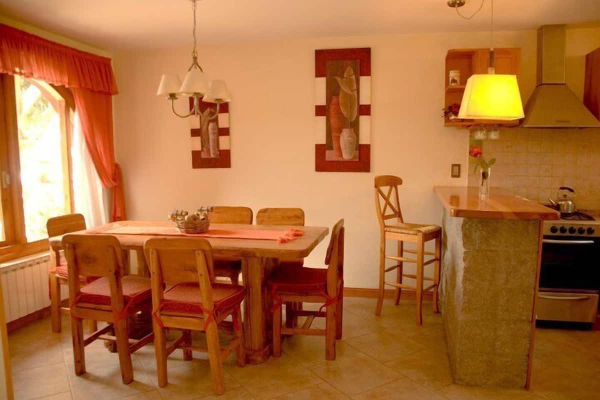 Un comedor con una mesa y sillas de madera, una cocina con estufa y alacenas, y obras de arte en las paredes.