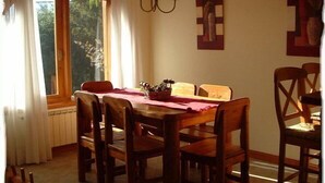 Un comedor con una mesa y sillas de madera, una araña y una ventana con cortinas.