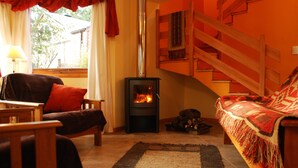 Una sala de estar acogedora con una chimenea de leña, un sofá, un sillón y una escalera.