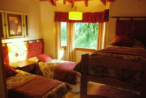 Une chambre avec deux lits simples, une tête de lit en bois, une table de chevet avec une lampe et une fenêtre avec des rideaux.