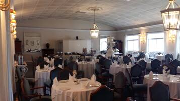 A formal dining room with multiple tables set for service, elegant chairs, and a high ceiling with decorative lighting.