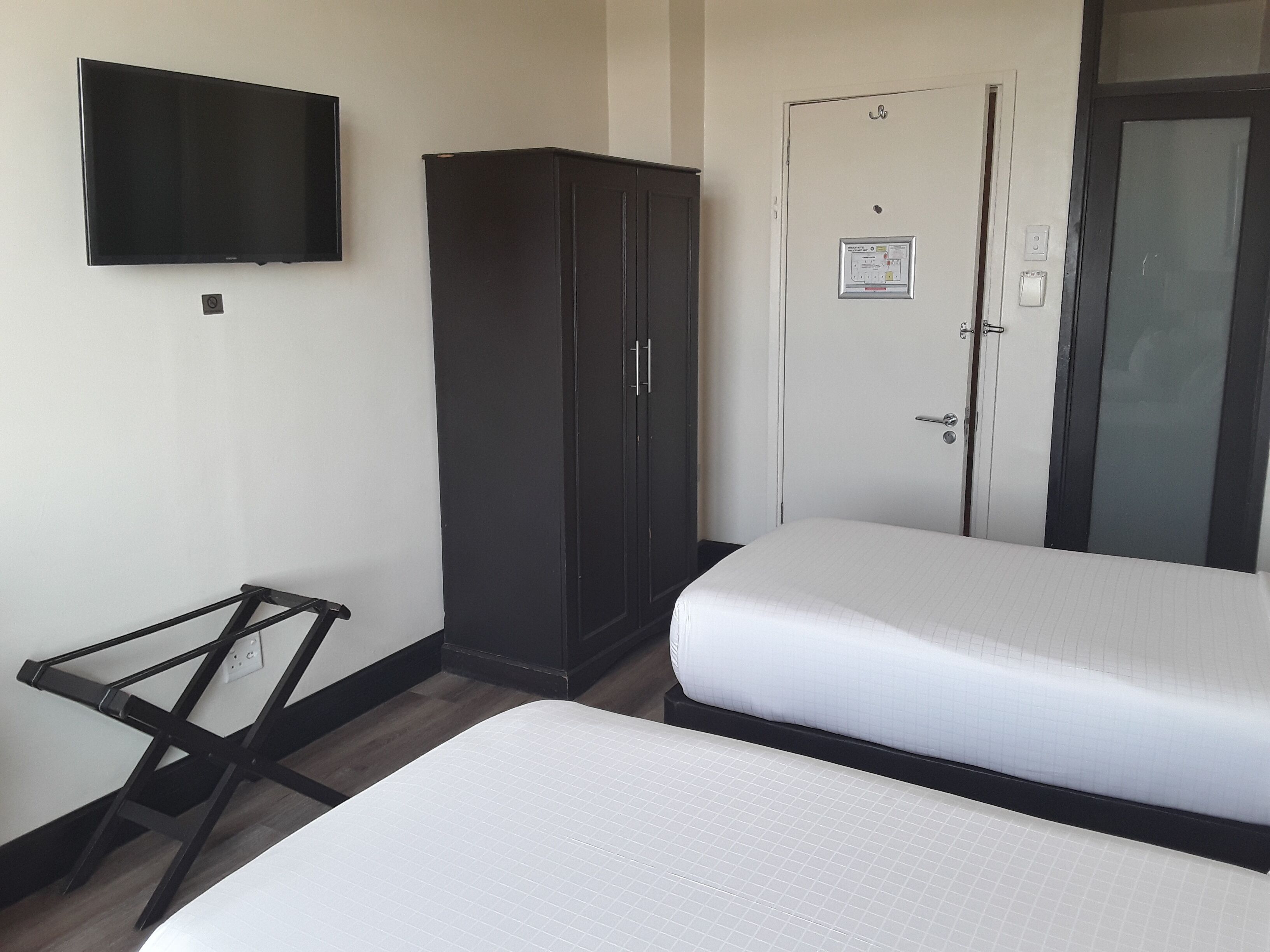 A hotel room with two beds, a wardrobe, a television, and a door with a notice.