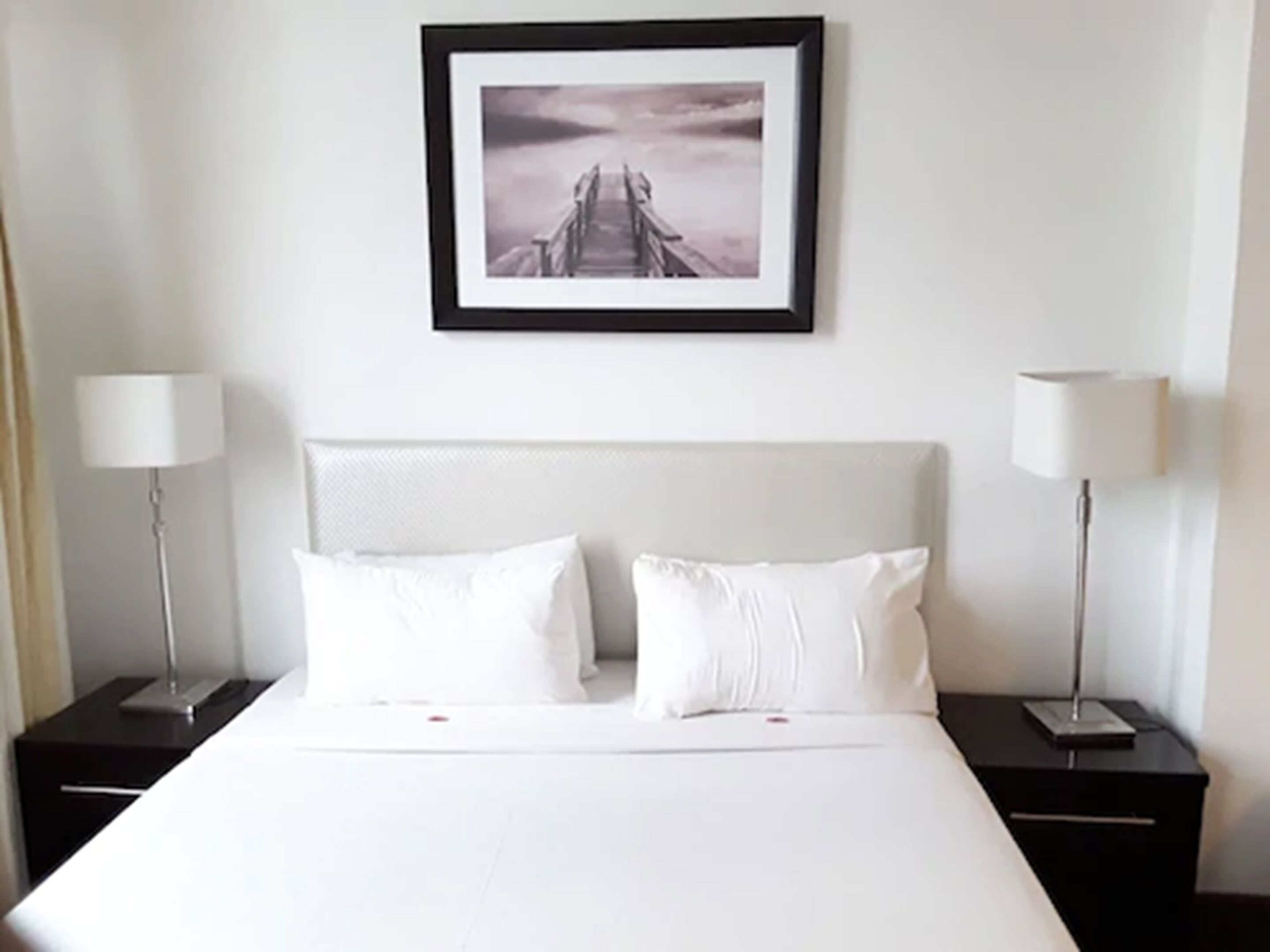 A hotel room with a large bed, two bedside tables with lamps, and a framed picture on the wall.