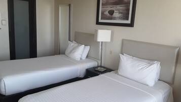 A hotel room with two beds, a nightstand with a lamp, a framed picture on the wall, and a door.