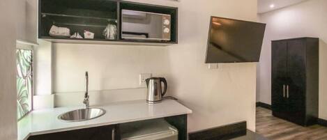 A compact kitchen with a built-in microwave, a kettle, and a small refrigerator.