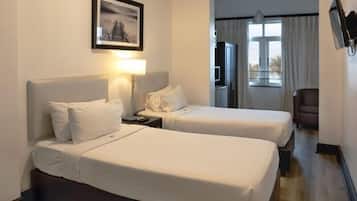 A hotel room with two beds, a desk with a lamp, a television, and a window with curtains.