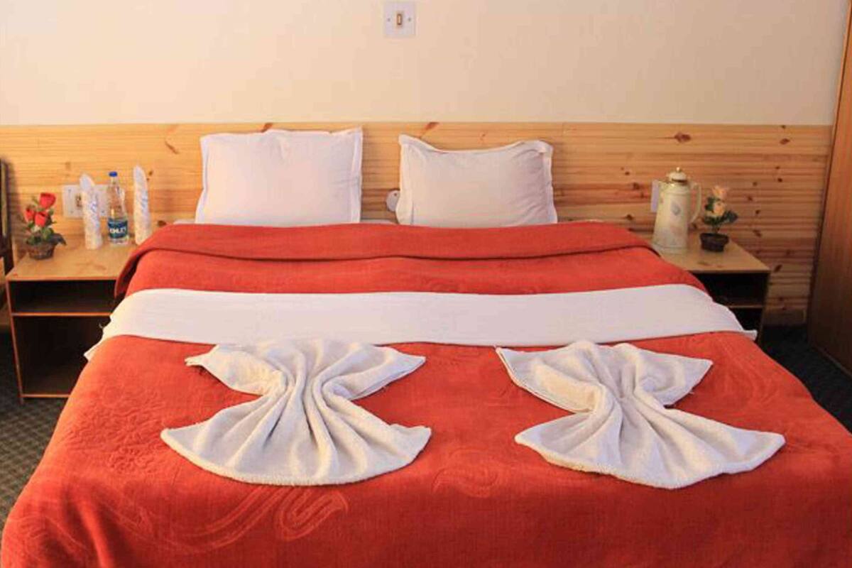 A hotel room with a wooden headboard, a red bedspread, white pillows, and a neatly made bed with towels.