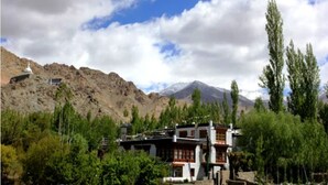 Un edificio tradicional con techo plano, rodeado de follaje y montañas al fondo.