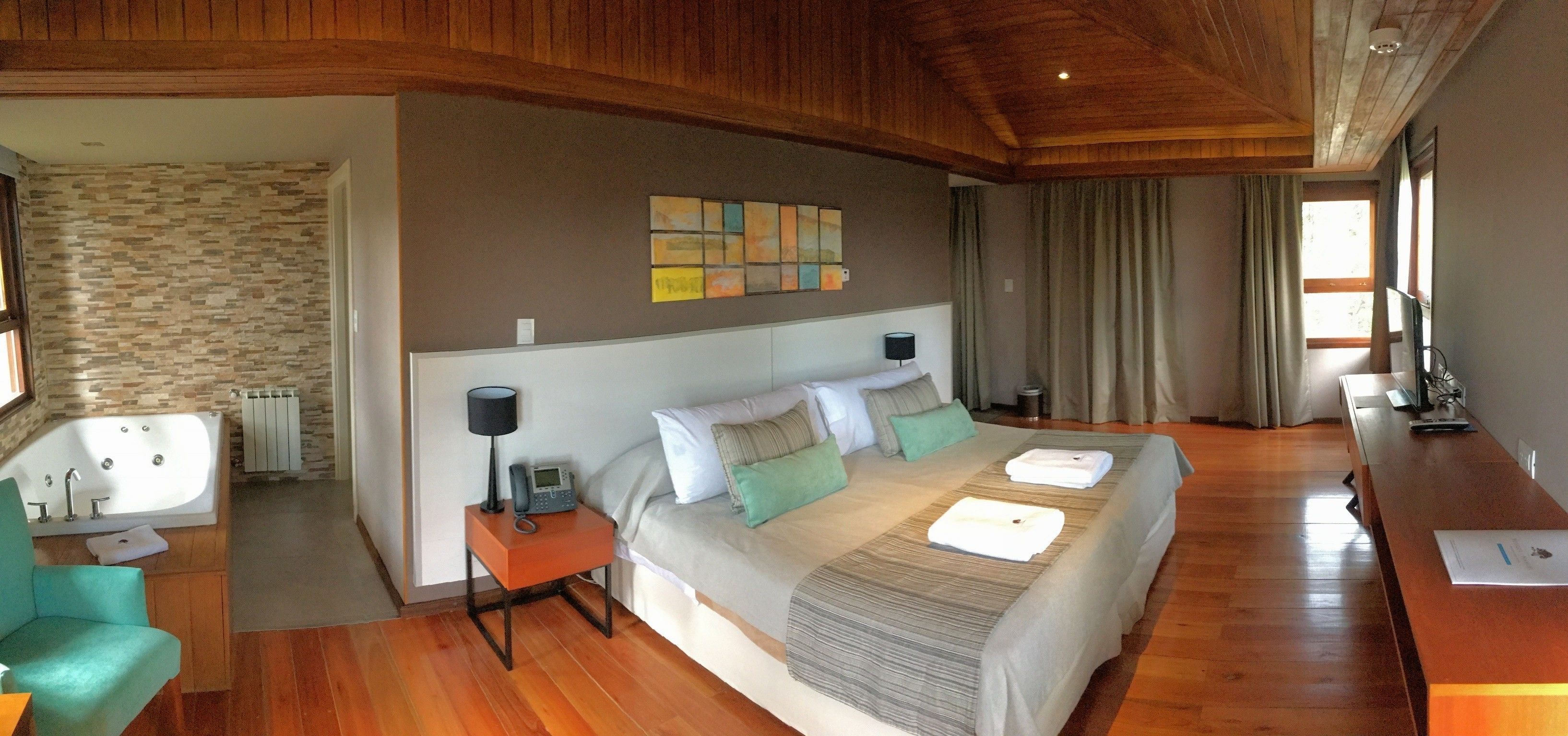 Quarto espaçoso com uma cama grande, mesa de cabeceira com abajur, banheiro com banheira e teto de madeira.