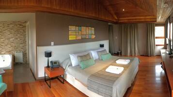 Quarto espaçoso com uma cama grande, mesa de cabeceira com abajur, banheiro com banheira e teto de madeira.