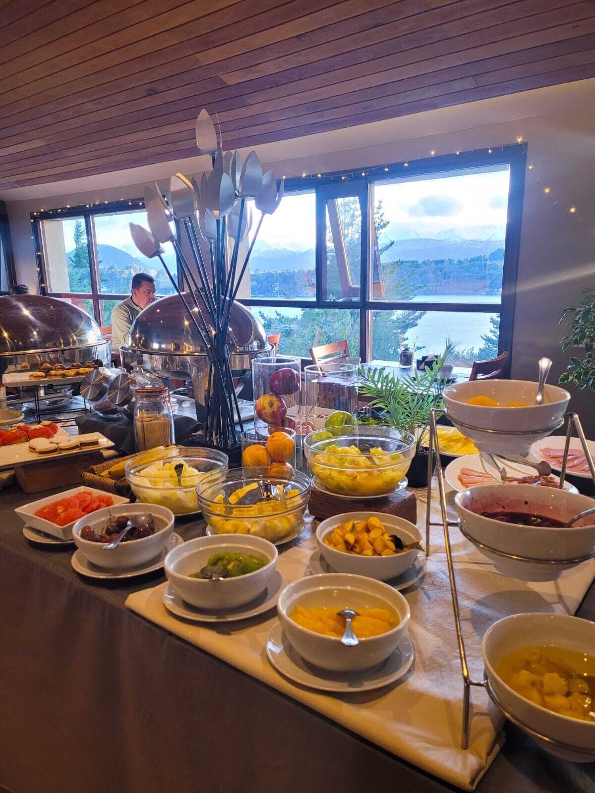 A buffet setup with various food items and a view of mountains through large windows.
